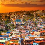 Expansive view of Valparaíso's colorful hillside homes at sunset, with the sun glowing orange over the Pacific — a popular artistic and coastal destination for expats moving to Chile from the US.