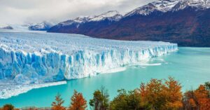 Massive ice wall of the Perito Moreno Glacier meeting turquoise waters, surrounded by fall foliage — a dramatic highlight of southern Argentina for adventurous expats.